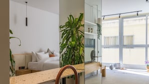 Una habitación de hotel moderna con una cama, un espejo grande, una planta y vistas al exterior.