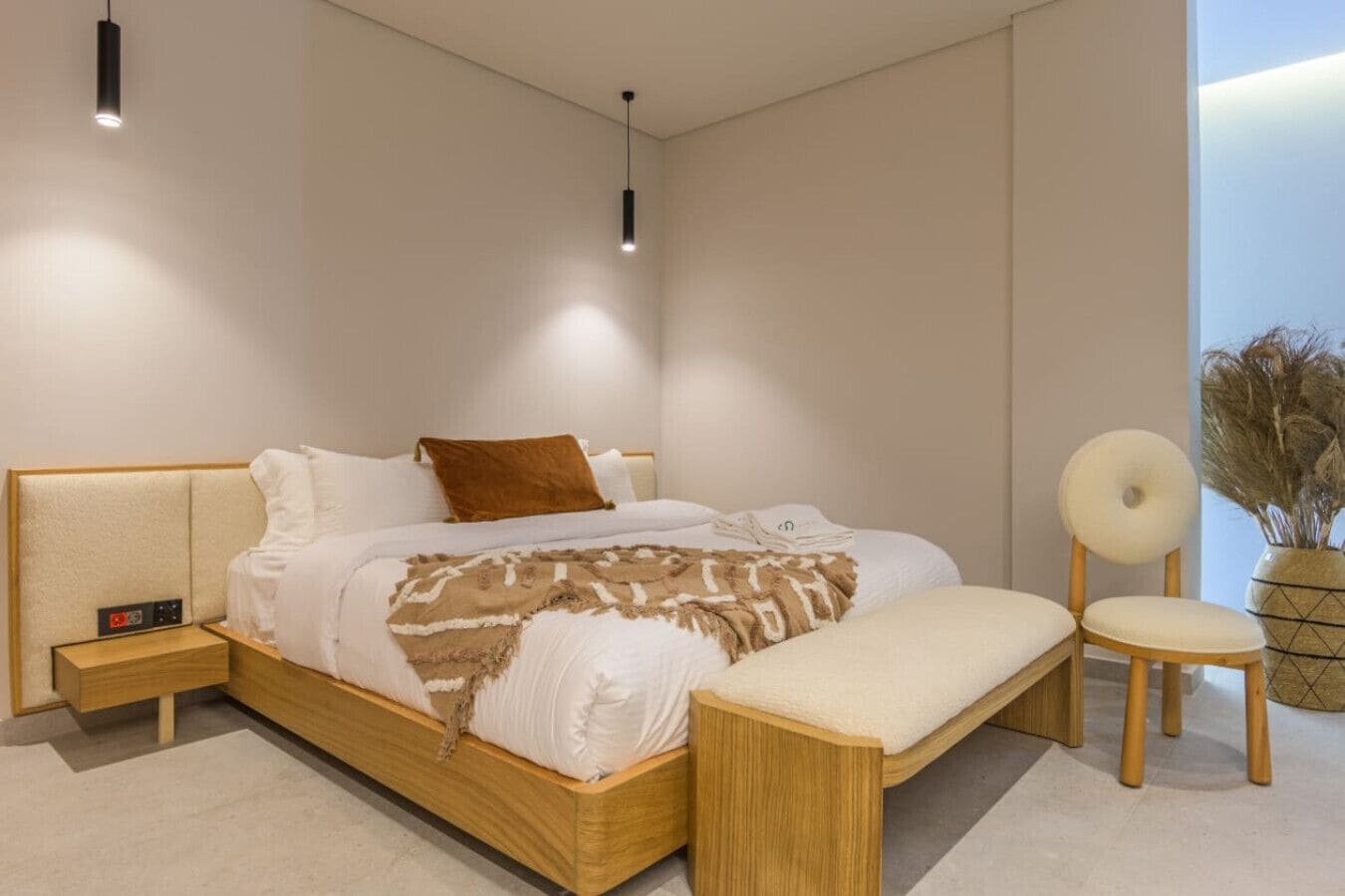 Une chambre à coucher moderne avec un lit en bois, des tables de chevet, un banc, une chaise et une plante en pot.