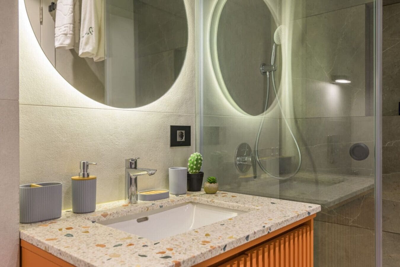 Un baño moderno con un espejo grande, un lavabo con encimera de mármol y una zona de ducha.