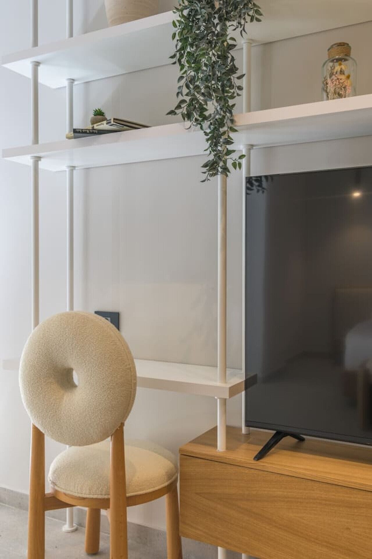 A modern living room with a flat-screen TV on a wooden stand, a round chair with a cushion, and a hanging plant.
