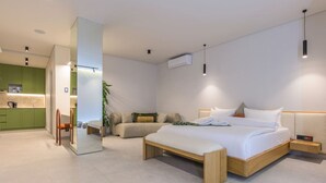 Una habitación de hotel moderna con una cama grande, una zona de estar con un sofá, una mesita y una cocina pequeña con detalles verdes.