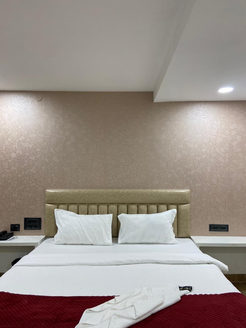 Quarto de hotel com cama, duas almofadas, manta vermelha e cabeceira bege.