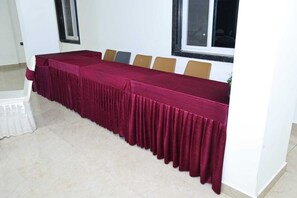 Una larga mesa con mantel rojo, sillas color beige y una ventana con persianas.