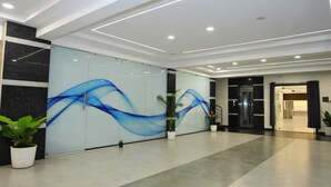 A modern lobby with a glass wall featuring blue wave patterns, potted plants, and a staircase leading to another area. - Hotel Vista Airport Zone (Hyderabad)