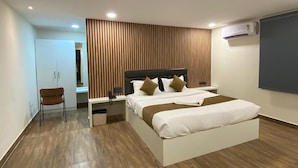 A modern bedroom with a large bed, a chair, a bedside table, and an air conditioning unit. - Hotel Vista Airport Zone (Hyderabad)
