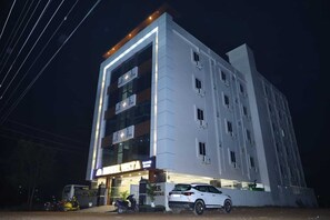 Un hotel de varios pisos con fachada moderna, señalización iluminada y un estacionamiento con varios veh ículos.