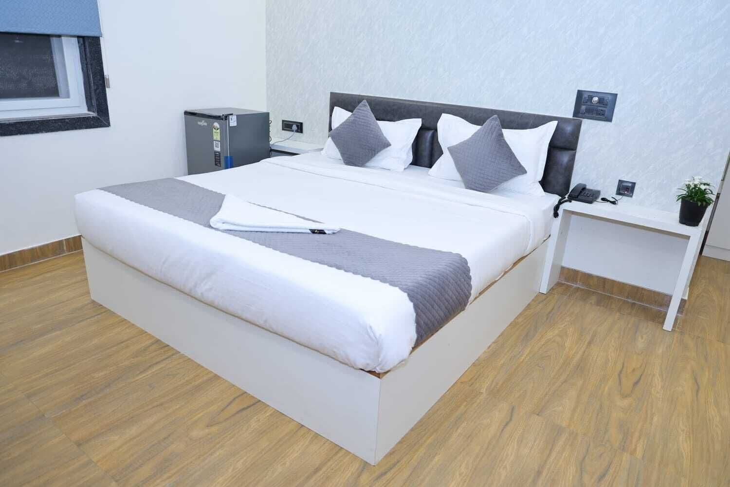 A modern hotel room with a large bed, a bedside table, a desk, and a small cabinet.
