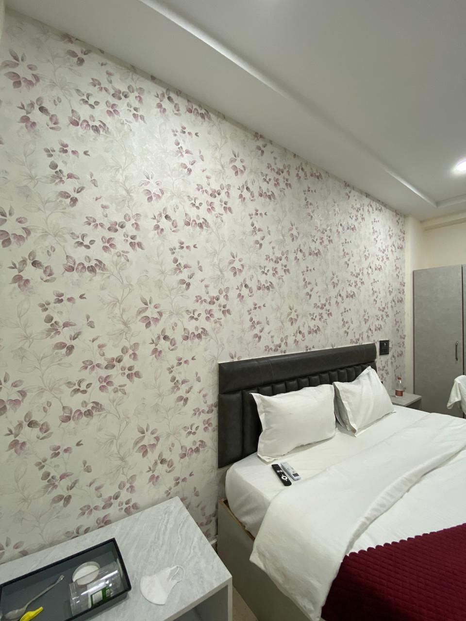 A hotel room with a floral wallpaper, a bed with white bedding, a nightstand with a toothbrush and a cup, and a wardrobe.