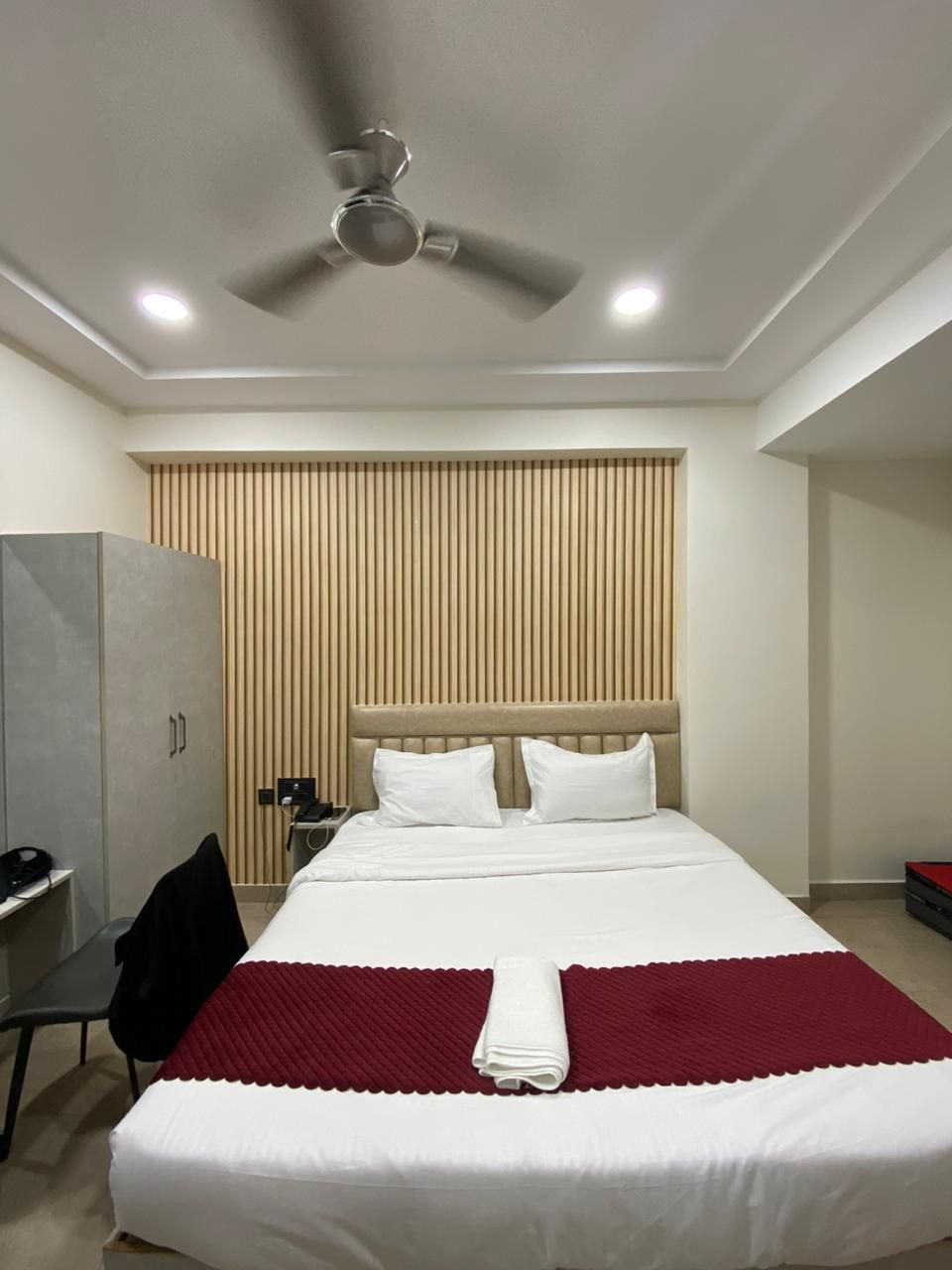 A hotel room with a bed, a desk, a wardrobe, and a ceiling fan.