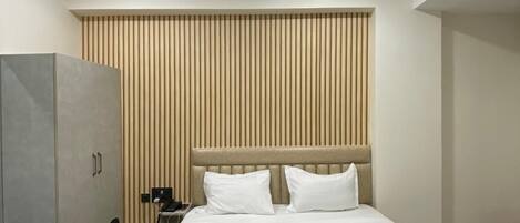 A hotel room with a bed, a desk, a wardrobe, and a ceiling fan.