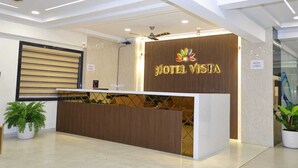 A modern hotel reception area with a reception desk, a large potted plant, and a sign displaying the hotel name. - Hotel Vista Airport Zone (Hyderabad)