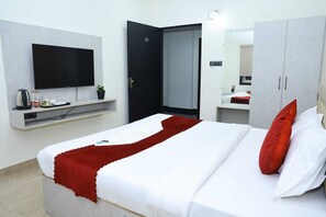 Habitación de hotel con cama, televisor montado en la pared, armario y una pequeña estantería con artículos de aseo.