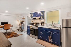 A modern kitchen with blue cabinets, stainless steel appliances, and a dining area with a wooden table and chairs. - The Dapper Den Suite (Atlanta)