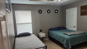 Un dormitorio con dos camas, una ventana con persianas, una mesita de noche con una planta y una puerta.