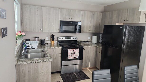 Una cocina moderna con armarios grises, una estufa negra, un microondas y un refrigerador negro.