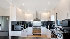 A modern kitchen with white cabinetry, a stainless steel range hood, and a built-in oven. - Metawise Luxe 6 Bed Ocean View Family Home in Seaforth (Sydney)