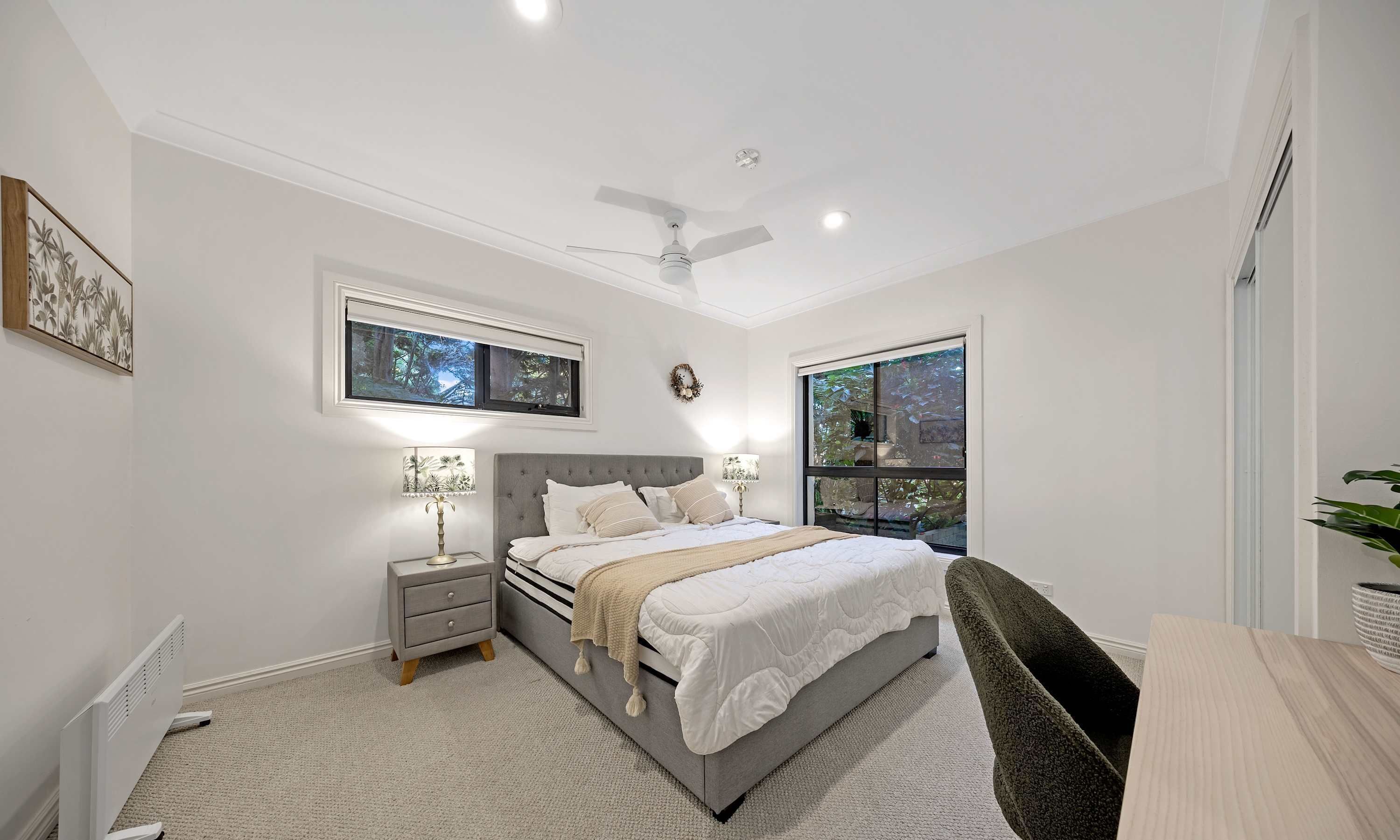 A bedroom with a bed, nightstands, a ceiling fan, and two windows.