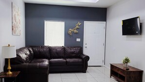 A modern living room with a dark-colored sofa, a small wooden side table, and a TV mounted on the wall. - Apartment With 3 Bedrooms 40 Minutes From South Padre (Weslaco)