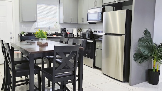 A modern kitchen with a dining area, featuring stainless steel appliances, grey cabinets, and a black dining table with chairs. - Apartment With 3 Bedrooms 40 Minutes From South Padre (Weslaco)