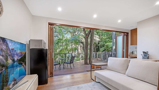 A modern living room with a large flat-screen TV, a black refrigerator, a beige sofa, and a wooden coffee table. - Metawisebnb Stylish Loft Studio With Garden in Seaforth (Sydney)