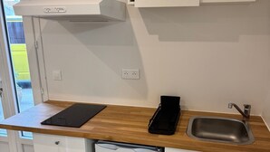 Et kompakt køkken med et GE Tech køleskab, en indbygget opvaskemaskine, en sort induktionskogetop og en stålvask.