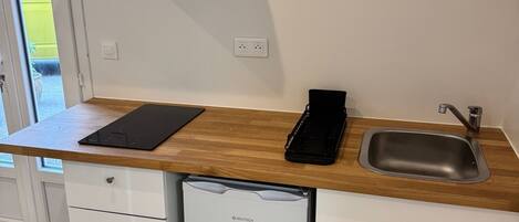 Eine kompakte Küche mit einem GE Tech Kühlschrank, einem eingebauten Geschirrspüler, einer schwarzen Induktionskochplatte und einer Edelstahl-Spüle.