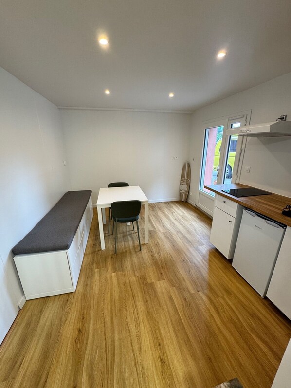 A compact kitchen with a dining area, white cabinetry, and a bench.