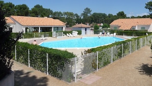 A swimming pool surrounded by a fence, with lounge chairs and a small building nearby.