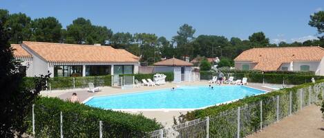 A swimming pool surrounded by a fence, with lounge chairs and a small building nearby.