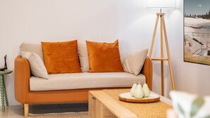 Una sala de estar con un sofá, dos cojines naranjas, una lámpara de pie y una mesa de centro con objetos decorativos.