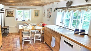 A kitchen with a wooden table, white chairs, a red pot, and a dishwasher.