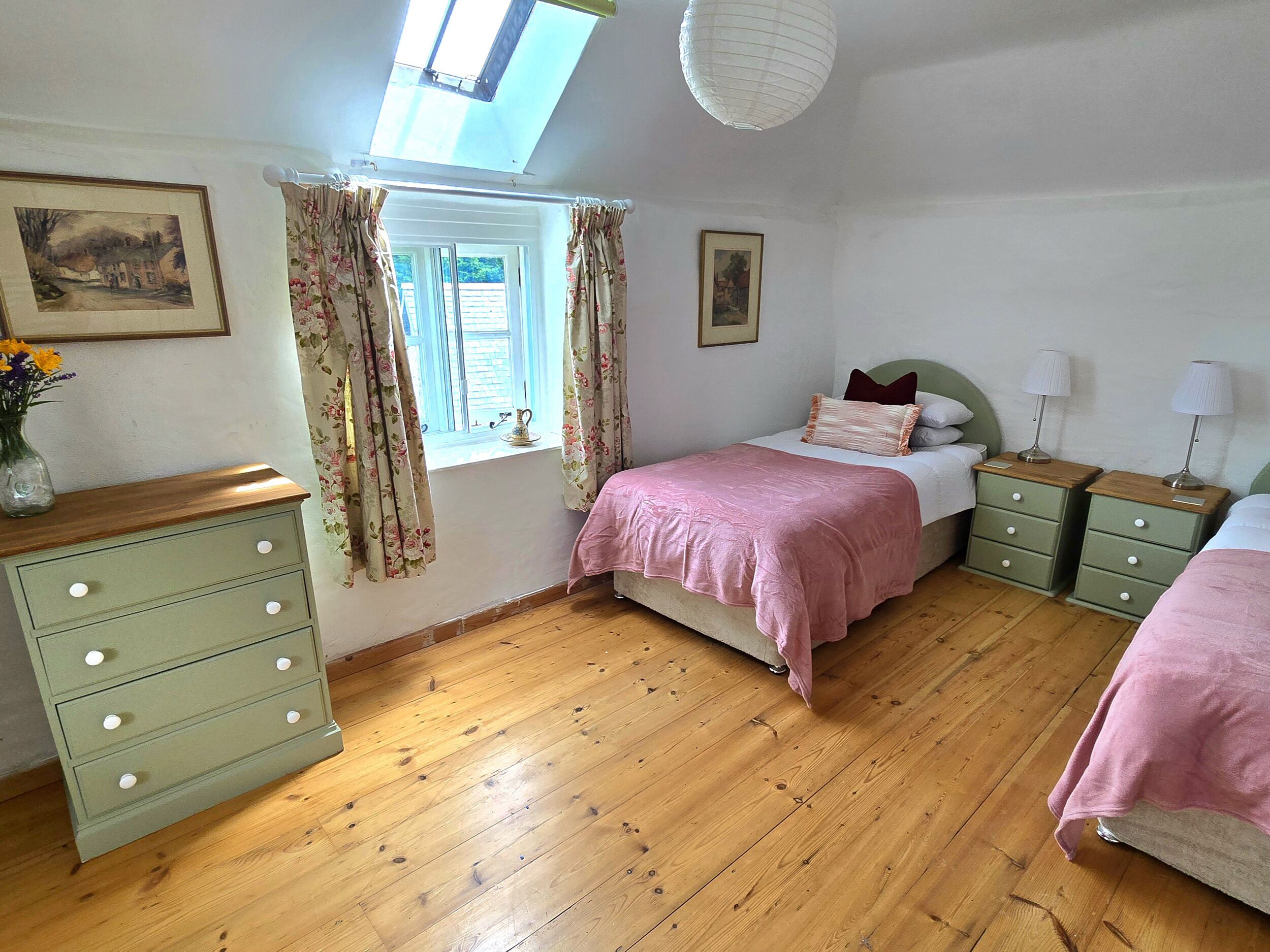 A bedroom with a bed, two nightstands with lamps, a dresser, a window with curtains, and a skylight.