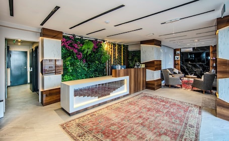 A modern reception area with a wooden reception desk, a green vertical garden, and a large flat-screen TV.