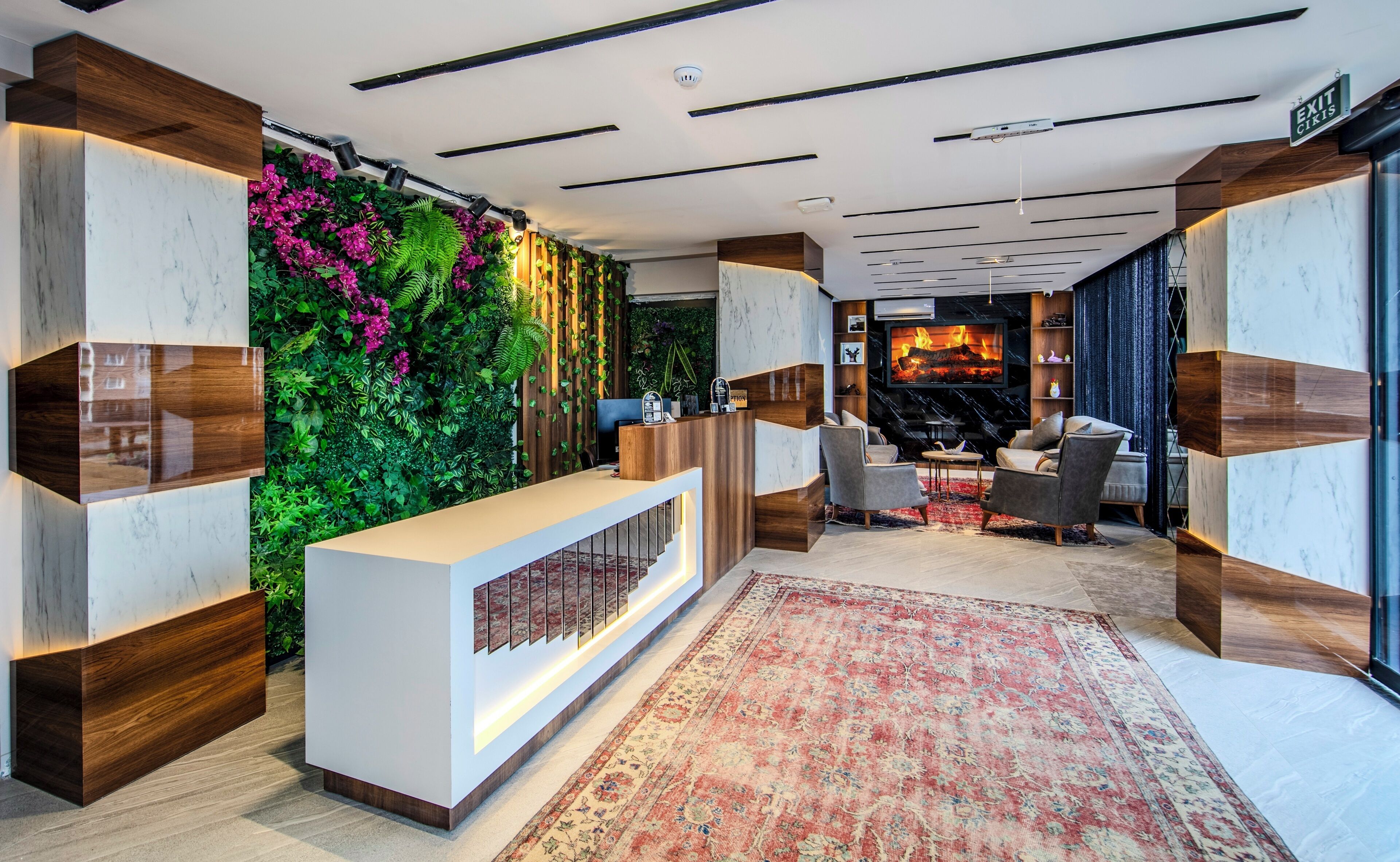 A modern reception area with a wooden reception desk, a green vertical garden, and a seating area with a fire feature.