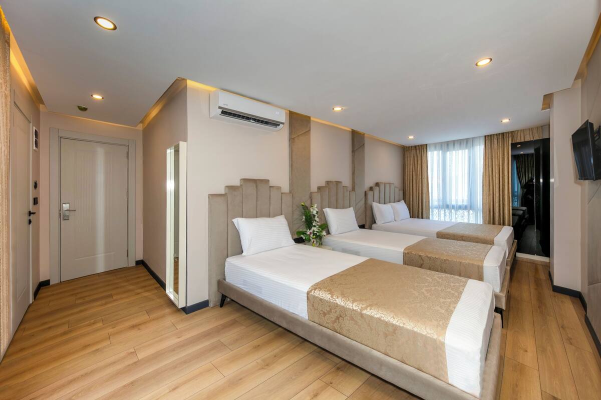 Ein Hotelzimmer mit zwei Betten, Holzboden, Deckenventilator und einem an der Wand montierten Fernseher.