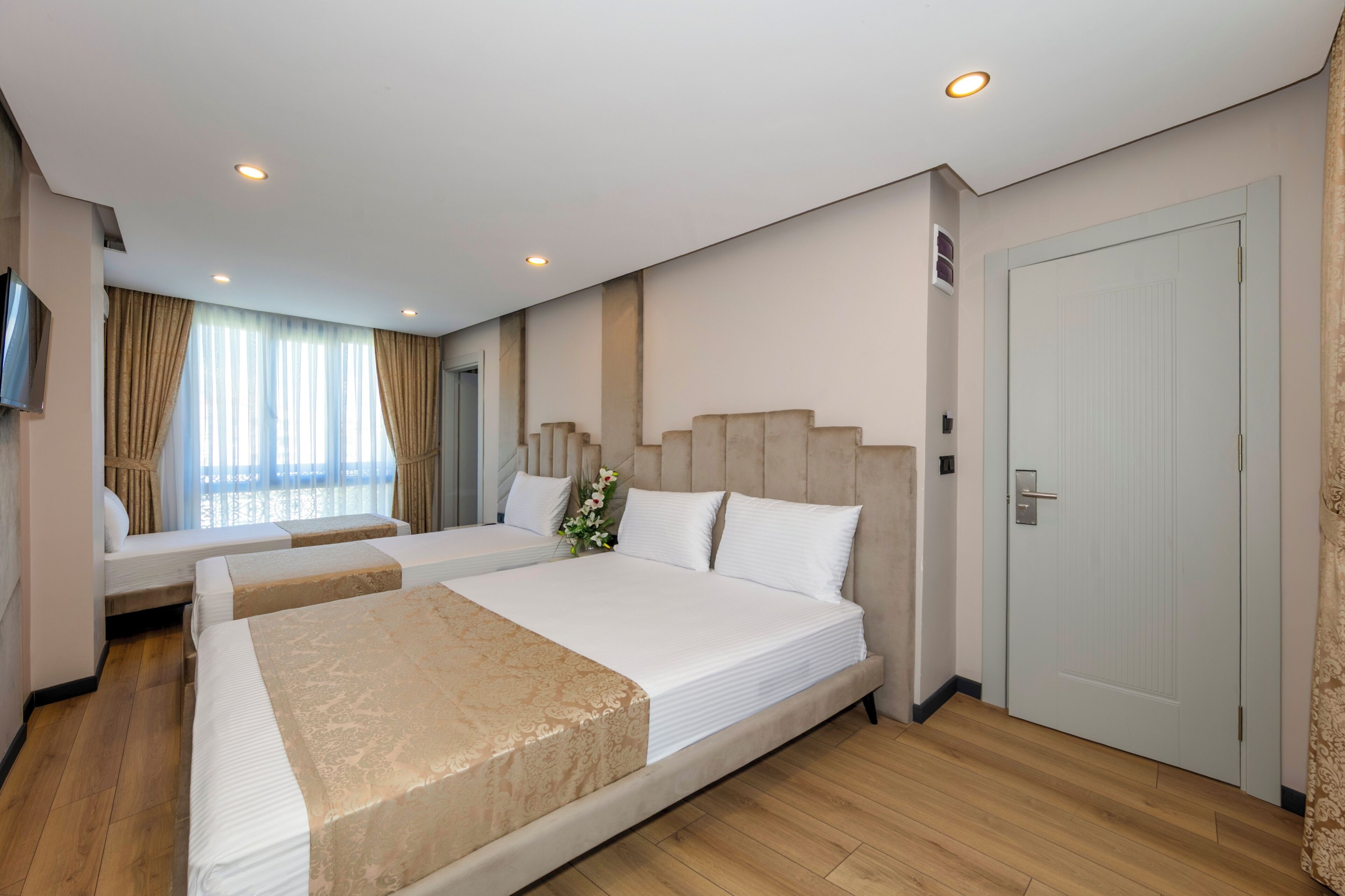 Une chambre d’hôtel avec un grand lit, un lit plus petit, un canapé, une télévision et une porte.