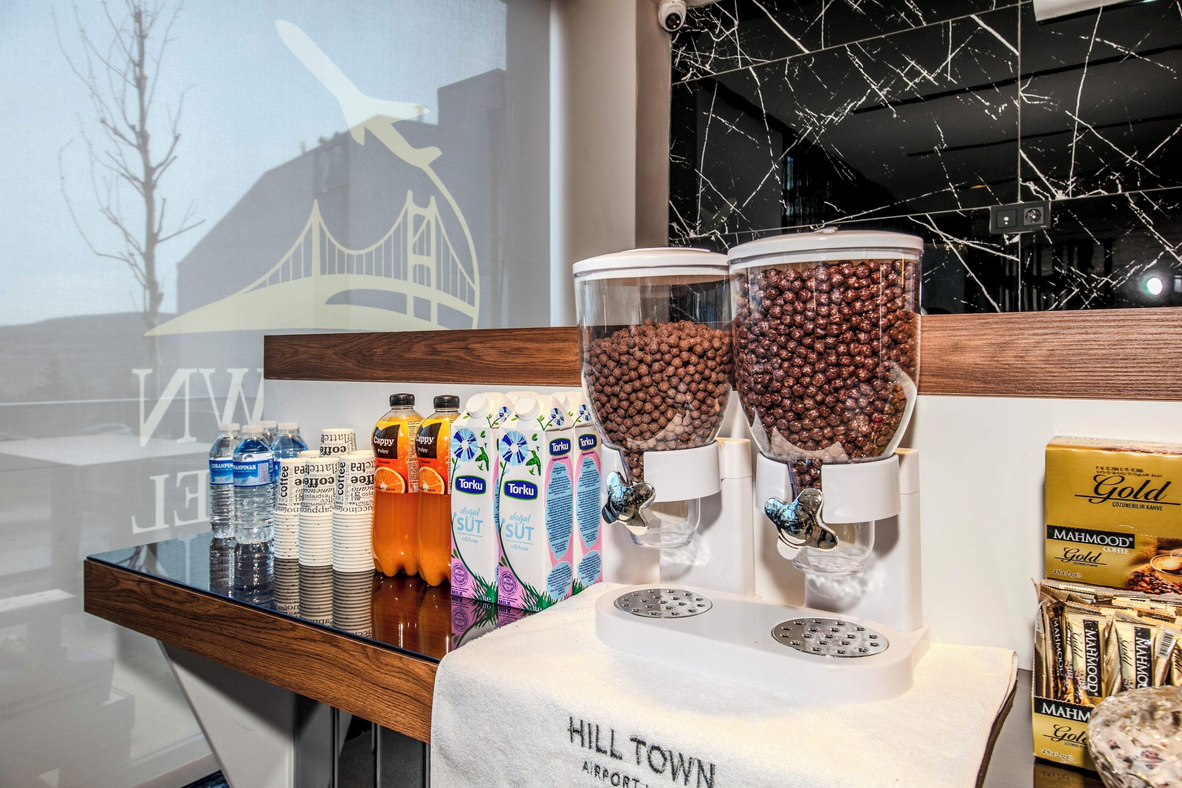 Una cafetera con dos dispensadores, una variedad de bebidas embotelladas y una caja de cápsulas de café sobre una mesa.