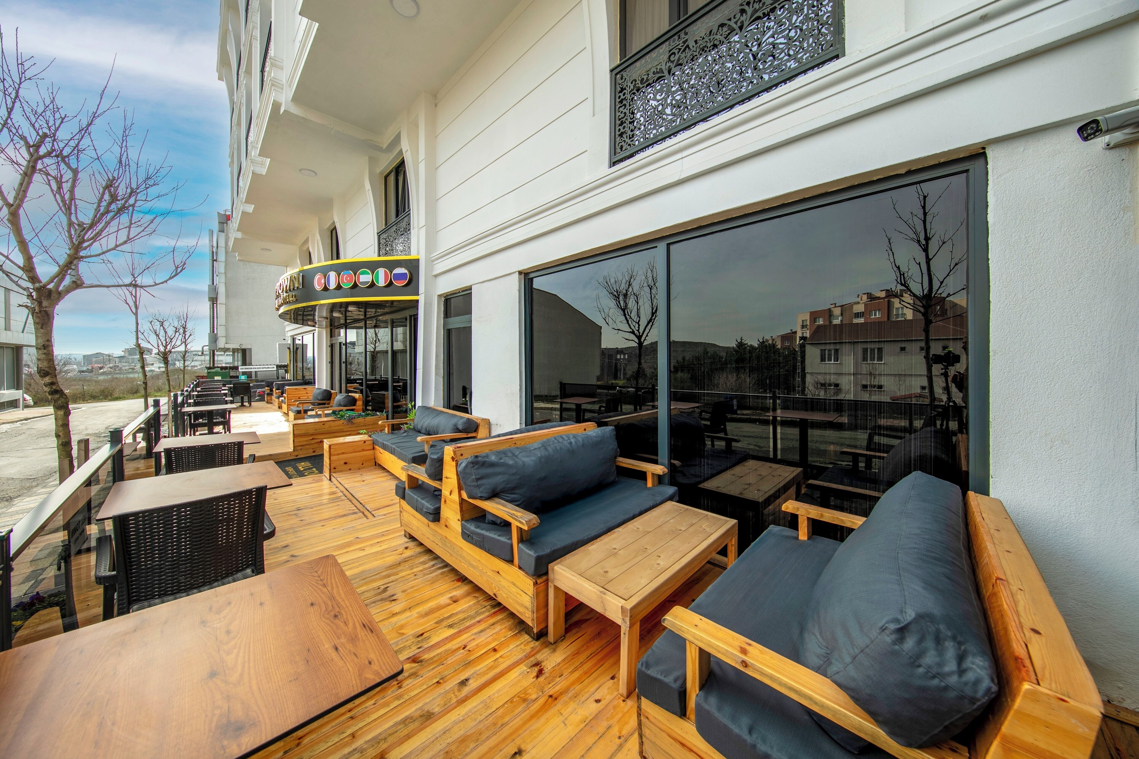 Een terras met houten meubels en grote ramen met uitzicht op een stadsbeeld.