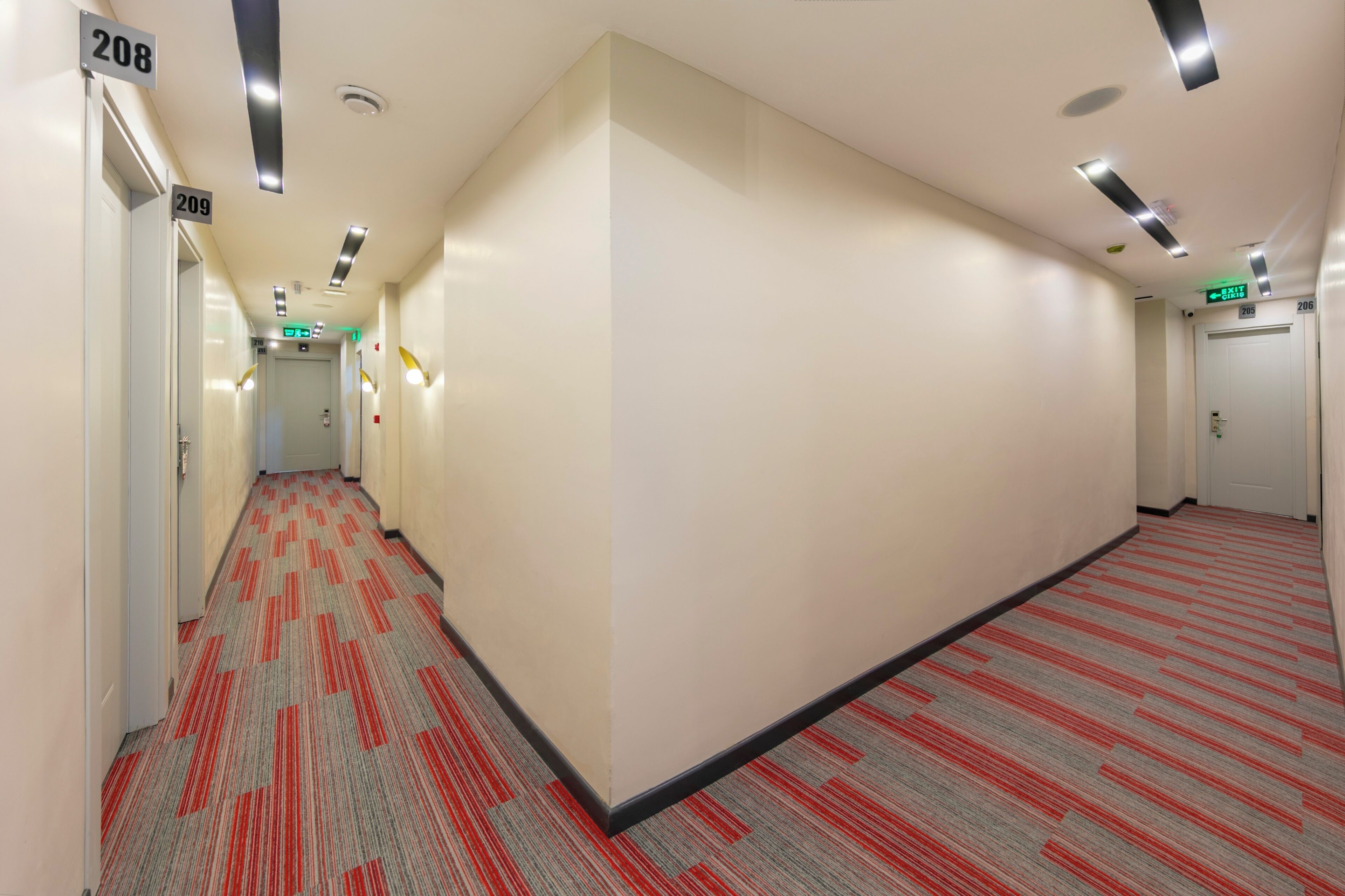 A hotel corridor with carpeted floors, white walls, and numbered doors.