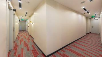 A hotel corridor with carpeted floors, white walls, and numbered doors.