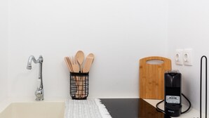 Een badkamer met een wastafel, kraan, houten keukengerei in een mand, een snijplank, en een aangesloten Krups koffiezetapparaat.