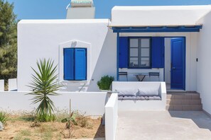 A white building with blue doors and shutters, a small outdoor seating area, and a staircase leading to the entrance. - Aitheras Luxury Suites (Paros)