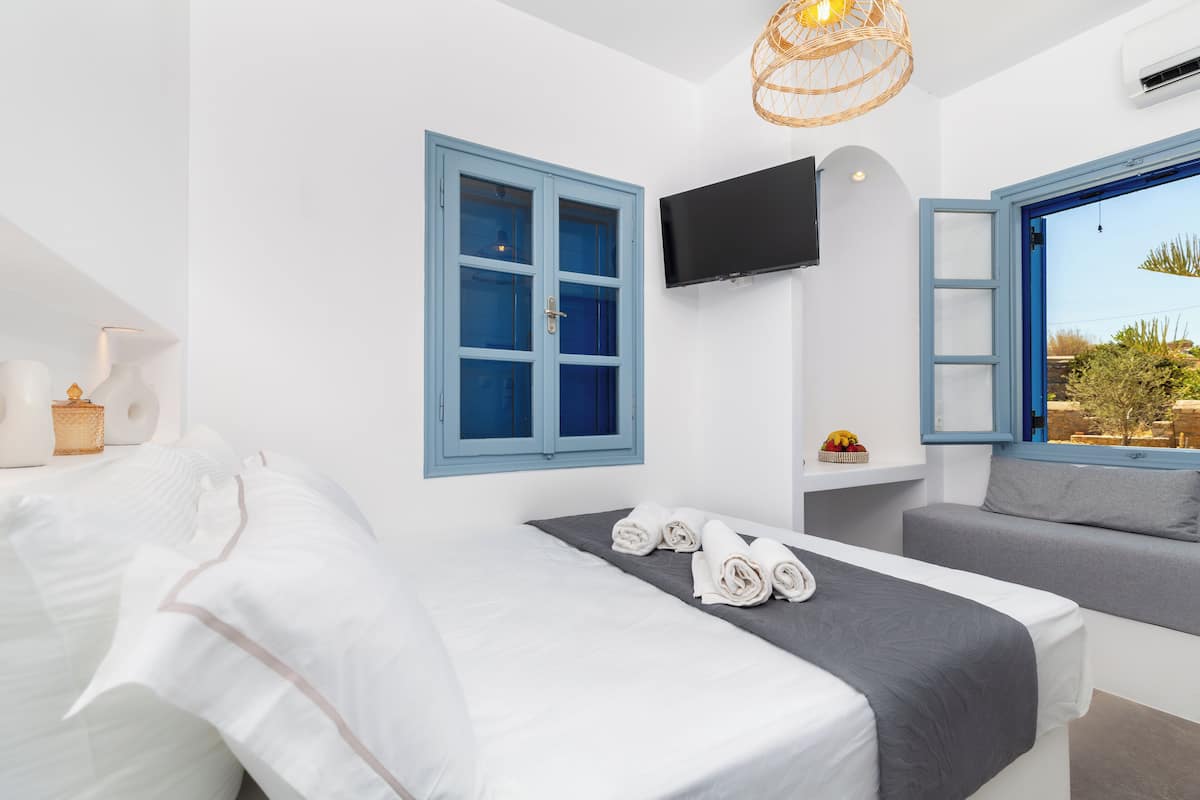 A hotel room with a bed, a TV mounted on the wall, and a window with an open door.
