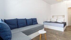 Een moderne slaapkamer met een grijze bank, een klein wit tafeltje en een bed met wit beddengoed.