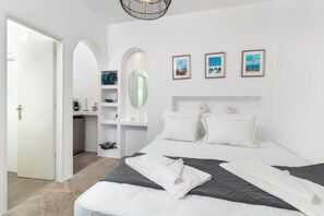 A modern bedroom with a large bed, a built-in wardrobe, a mirror, and three framed pictures on the wall. - Aitheras Luxury Suites (Paros)
