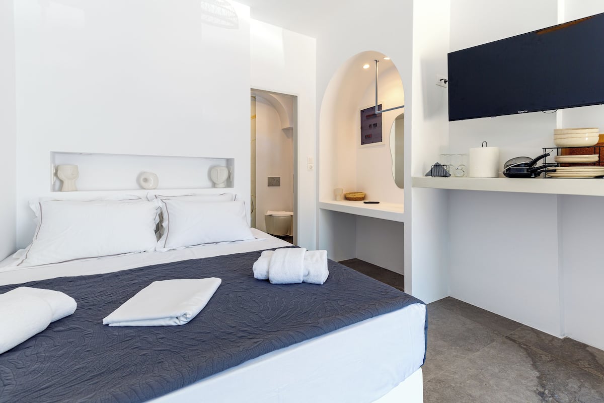 A modern hotel room with a neatly made bed, a flat-screen TV mounted on the wall, and a small shelf with toiletries.