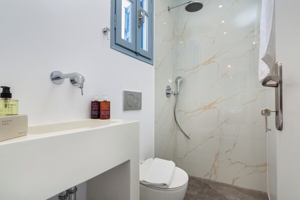 A modern bathroom with a white vanity, a shower with a glass door, and a toilet. - Aitheras Luxury Suites (Paros)