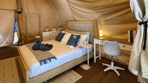 A cozy tented accommodation with a bed, bedside table, chair, and a small desk with a lamp. - Reef Resort Unit B8 (Island Garden City Of Samal)