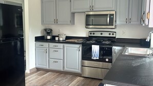 A kitchen with grey cabinets, a black refrigerator, a microwave, an oven, and a wooden floor. - Sunnyside Suite in peaceful Cambridge Springs (Cambridge Springs)