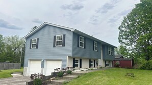 A two-story residential house with a garage, a front yard with a small garden, and a red barn in the background. - Sunnyside Suite in peaceful Cambridge Springs (Cambridge Springs)
